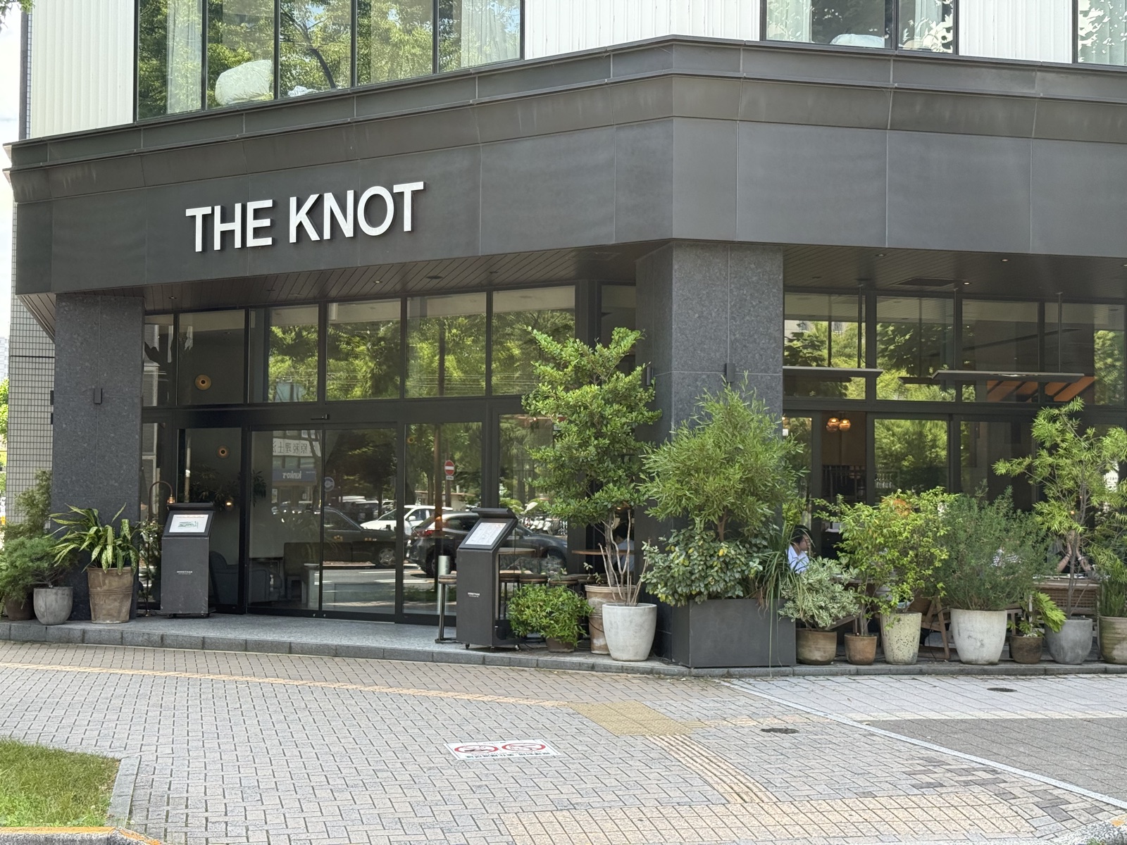 The Knot Hiroshima exterior — a sleek dark-toned hotel entrance lined with planters
