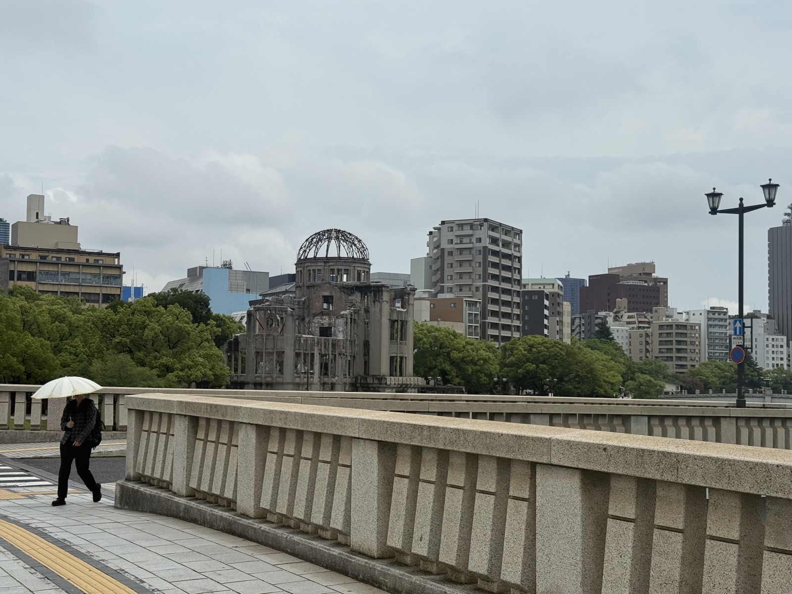 Woman with umbrella walks past Hiroshima Peace Park in rain