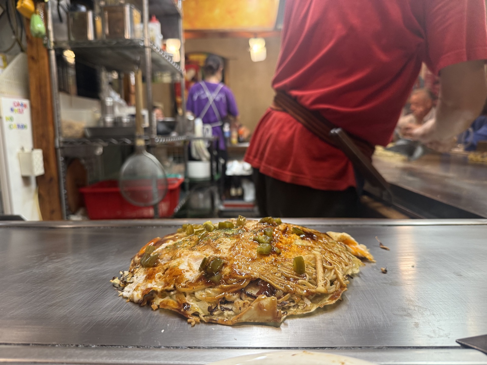 Chef preparing okonomiyaki on griddle in Hiroshima restaurant